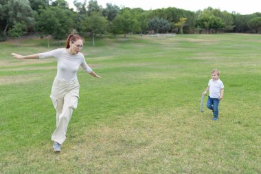 Anne, oğluyla çimenli bir parkta oynarken uçak gibi davranıyor.