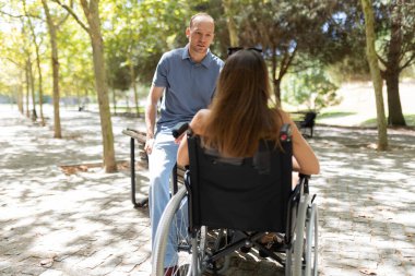Kadın ve erkek parkta sohbet ediyorlar, engelli insanlara ilgi ve destek gösteriyorlar.