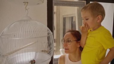 Anne ve çocuk kafesteki küçük kuşu izliyor.
