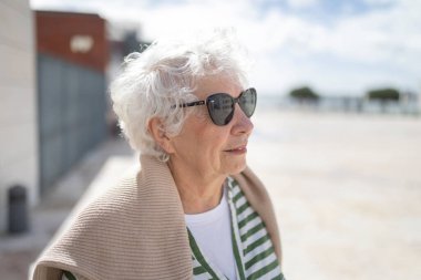 Güneş gözlüğü takan, gözlerini kaçıran, güneşli bir günün tadını çıkaran son sınıf bir kadının portresi.