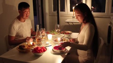 Sevgi dolu bir çift evde pasta, mumlar ve kalpten bir kutlamayla romantik bir doğum günü yemeği yiyor.