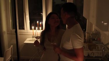 Romantik bir akşamın tadını çıkaran, şarap içen ve mum ışığında öpüşen çift.