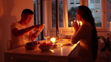 Mum ışığında romantik akşam yemeğinin tadını çıkaran bir çift, şarap dolduran bir adam.