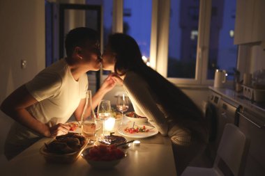 Genç çift mum ışığında romantik bir akşam yemeği yiyor, yemeklerini yerken öpüşüyorlar.
