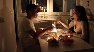 Genç çift mum ışığında romantik bir akşam yemeğini mutfak masasında paylaşıyor.