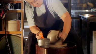 Yaşlı bir kadın, tekerleğin üzerinde ıslak kilden bir kap yapıyor. Orta çekim