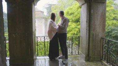 Bekleyen anne babalar güzel bir bahçeye tepeden bakan bir balkonda öpüşürken sevgi dolu bir anı paylaşıyorlar.