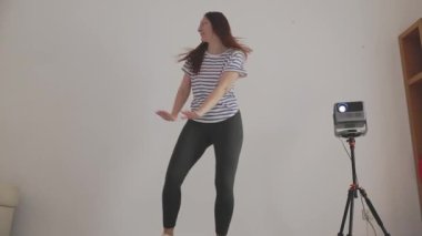 Kadın dans hareketleri yapıyor, kendini projektörle kaydediyor.