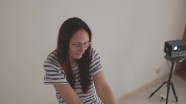 Enerjik kadın evde dans hareketleri yapıyor, duvardaki online öğretim programının ardından.