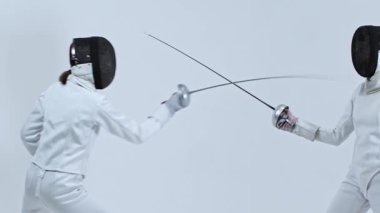 Beyaz takım elbiseli iki genç eskrimci arasında beyaz stüdyoda eskrim eğitimi. Orta çekim