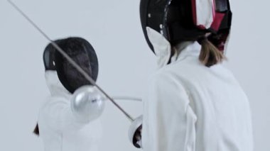 Eskrim. Beyazlar içindeki iki genç kadın eskrimci dövüşü eğitiyor. Orta çekim