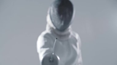 Eskrim. Beyaz takım elbiseli genç kadın eskrimci. Kılıçla kameraya nişan alıyor. Orta çekim