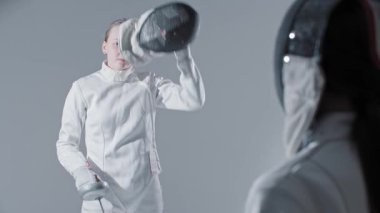 Eskrim - iki genç kadın eskrimci koruyucu kasklarını takıp antrenman maçı için birbirlerinin önünde duruyorlar. Orta çekim