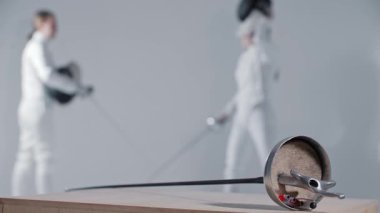 Eskrim - iki genç kadın eskrimci antrenman yapıyor - ön planda bir rapier. Orta çekim