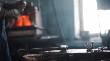 Kırmızı sıcak metalden gül döven metal işçisi bir atölyede örs üzerinde aletler kullanıyor.