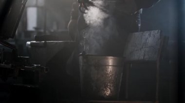 Metal işçisi sıcak bir metal parçasını su kovasında soğutarak buhar üretiyor.