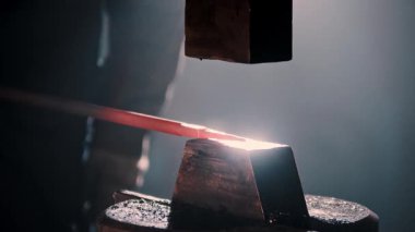 Güç çekici sıcak metali örse çarpıyor, kıvılcım ve duman yaratıyor.