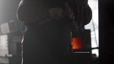 Demirci çekiç ve örsle loş ışıklı atölyede çalışıyor.