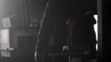 Demirci çekiç ve örsle loş ışıklı atölyede çalışıyor.