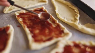 Şef dikdörtgen hamur parçalarına çilek reçeli sürüyor, hamur işlerini pişirme çarşafında hazırlıyor.