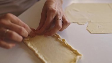 Pasta şefi beyaz bir masada dikdörtgen hamurla sınır çiziyor.