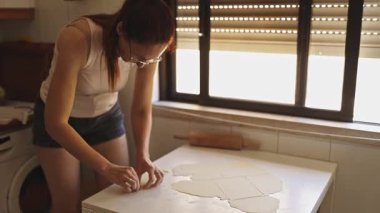 Kızıl saçlı kadın mutfakta beyaz bir masada puf böreği hazırlıyor.