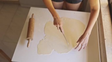 Kadın hamur hazırlıyor, beyaz bir masada üçgen şeklinde kesiyor.