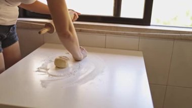 Kadın un serpiyor, hamuru yuvarlıyor ve beyaz masaya iğne takıyor.