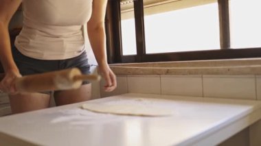 Kadın aydınlık bir ev mutfağında turta pişirmek için hamur hazırlıyor.