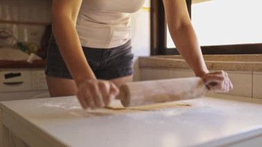 Beyaz bir masada merdaneyle hamuru düzleştiren kadın