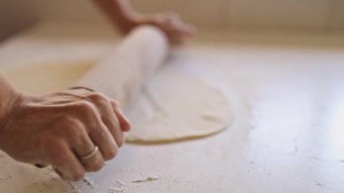 Beyaz bir masada hamuru hazırlayan dişi fırıncı, tahta bir oklavayla.