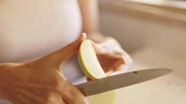 Ahşap kesme tahtasındaki bıçakla yeşil elmayı soyan kadın.