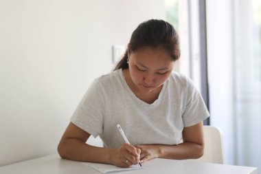 Asyalı etnik kökenli kız öğrenci ya da girişimci not alıyor, okuyor ya da evden çalışıyor