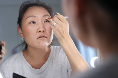 genç kadın bir ayna önünde bir fırçayla makyaj uygulamak