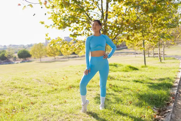 Genç Asyalı kadın mavi spor giyip parkta poz veriyor.