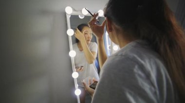 Asyalı kadın elinde ampullerle aynanın önüne göz farı sürüyor.