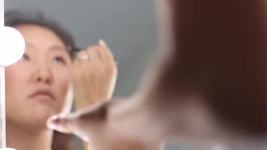 Aynanın önünde ampullü kaş kalemi kullanan Asyalı kadın.