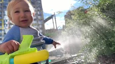 Mutlu bebek parkta güneşli bir günde su tabancasıyla oynuyor.
