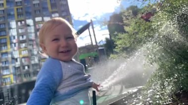Parkta bahçe hortumuyla oynayıp sıçrayan mutlu çocuk.