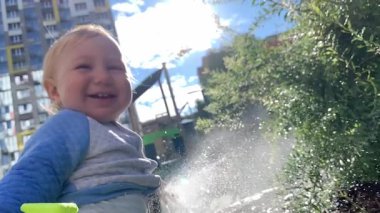 Mutlu erkek bebek su hortumuyla oynamayı, su sıçratmayı ve dışarıda eğlenmeyi seviyor.