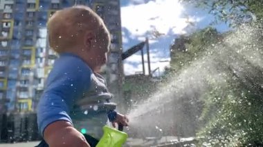 Sevimli erkek bebek su tabancasıyla oynamayı, güneşli şehir parkında su sıçratmayı seviyor.