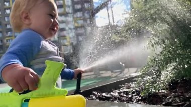 Güneşli bir yaz gününde şehir parkında su tabancasıyla oynayan mutlu çocuk.