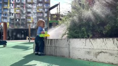 Mutlu çocuk su tabancasıyla oynuyor, bahçedeki bitkileri suluyor.