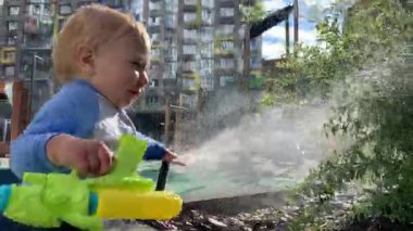 Mutlu çocuk su tabancasıyla oynuyor, güneşli bir günün tadını çıkarıyor.