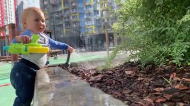 Küçük çocuk şehir parkında bitkileri oyuncak su tabancasıyla suluyor.