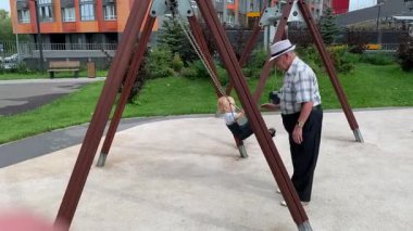 Yaşlı adam torununu nazikçe salıncakta sallıyor.