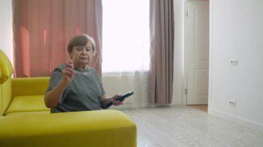 Son sınıf öğrencisi kadın rahat bir koltukta oturuyor, televizyon izliyor, kanal değiştiriyor, gözlüklerini ayarlıyor ve boş zamanlarının tadını çıkarıyor.