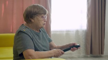 Yaşlı kadın televizyon izlerken uzaktan kumanda kullanıyor