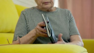 Yaşlı kadın rahat sarı bir kanepede dinleniyor, kitaptan zevk alıyor ve gözlüklerini çıkarıyor.