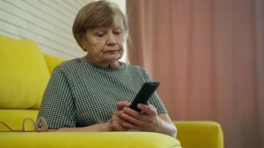 Üst düzey kadın televizyon izlerken uzaktan kumanda kullanıyor, kanal değiştiriyor ve sesi ayarlıyor.